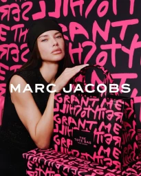 Model Adriana Lima wearing a black beanie and top next to a Marc Jacobs graffiti tote bag against a pink and black backdrop