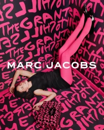Model Adriana Lima in a black dress and pink tights lying against a graphic graffiti wall for Marc Jacobs x Stephen Sprouse.