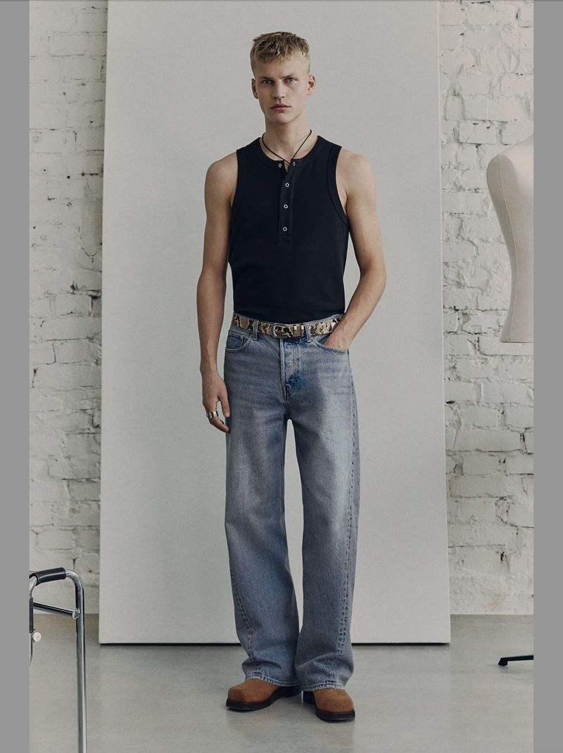 Full-length studio shot of a fair-skinned young adult male with blond hair, wearing jeans and a tank top, with a neutral facial expression.