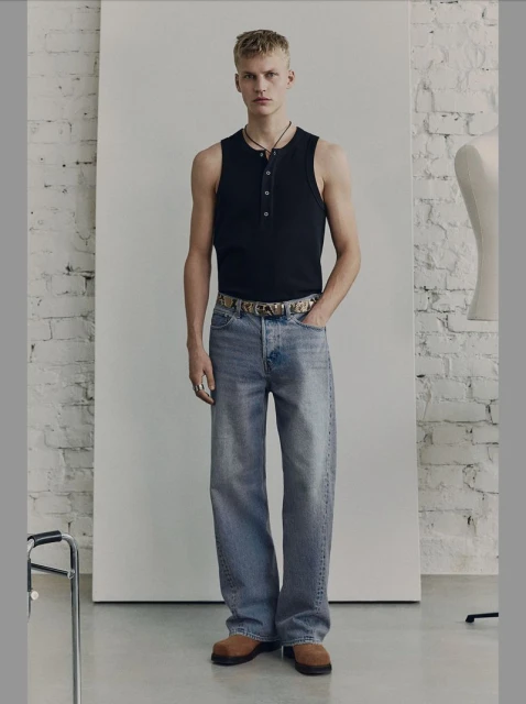 Full-length studio shot of a fair-skinned young adult male with blond hair, wearing jeans and a tank top, with a neutral facial expression.