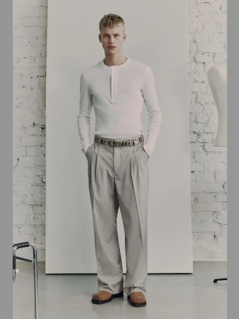 Model standing in white long-sleeve henley shirt and grey trousers against a studio backdrop