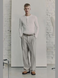 Model standing in white long-sleeve henley shirt and grey trousers against a studio backdrop