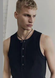 Close-up portrait of a male model wearing a black ribbed tank top with silver snaps against a plain studio background.