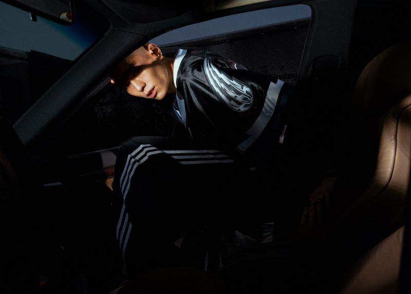 Man in a car interior wearing an Adidas track suit and jacket, creating a dark, moody, and enclosed atmosphere with limited light.