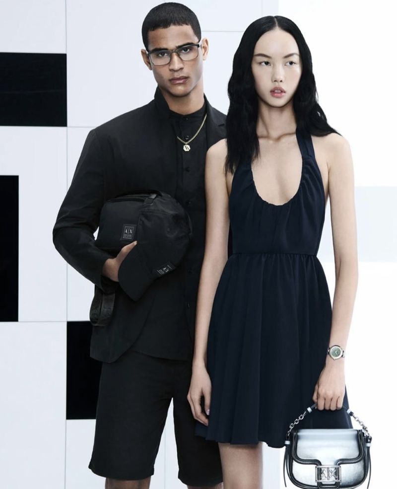 A fashionable couple poses in front of a geometric background, showcasing stylish clothing, accessories, and modern apparel for a fashion-forward aesthetic.