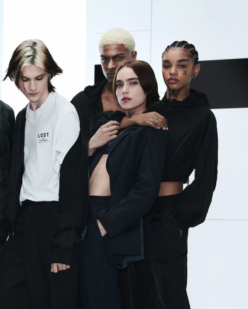 Four fashion models pose in black and white clothing against a modern monochrome background, showcasing contemporary style.