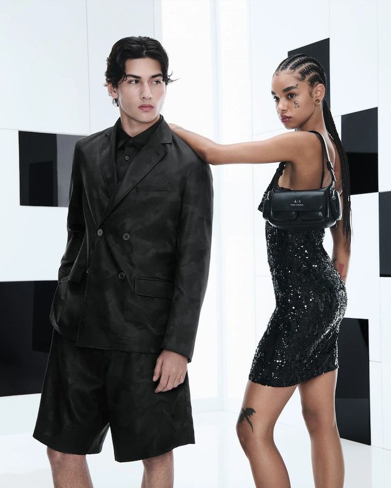 Two models wearing dark attire pose against a stark white studio backdrop featuring geometric black panels.