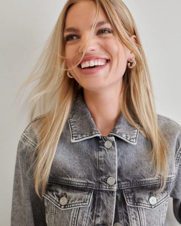 Smiling blond female model wearing a grey denim jacket against a neutral backdrop