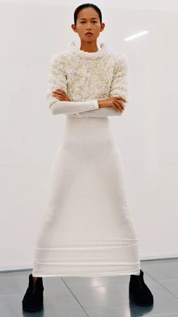 Full shot of a slender, Asian-appearing woman in a textured white top, long white skirt, and black shoes, posing against a white background.