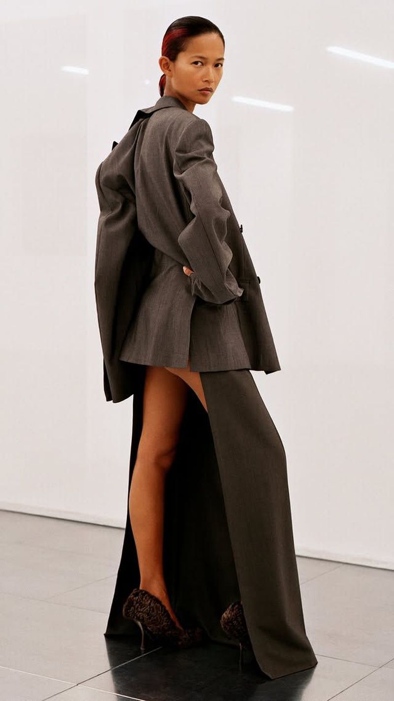 Elegant adult female fashion model in a gray jacket dress, posing in a photo studio, against a white backdrop and wearing leopard print heels.