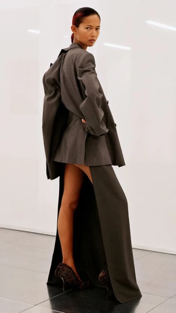 Elegant adult female fashion model in a gray jacket dress, posing in a photo studio, against a white backdrop and wearing leopard print heels.