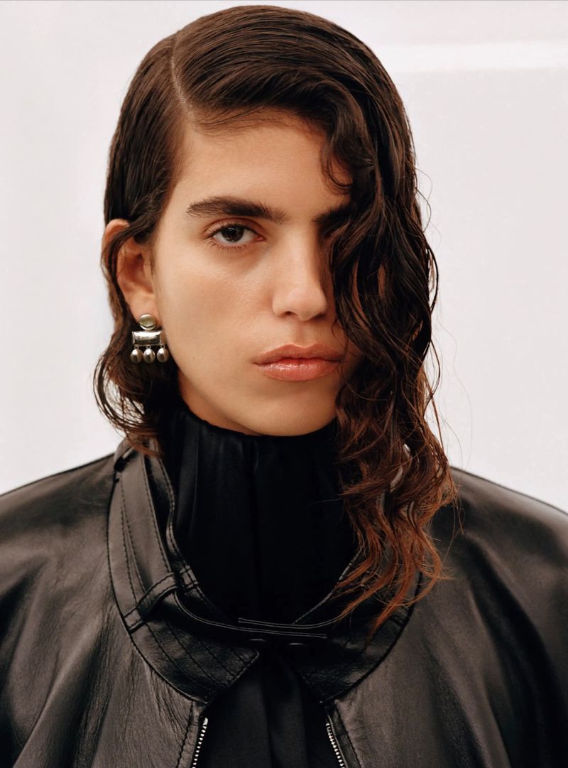 Portrait of a model wearing a black jacket and silver earrings against a plain white background