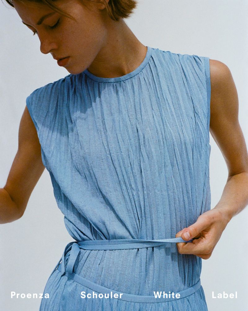 Model wearing a blue sleeveless pleated dress with a matching tie belt against a plain white background