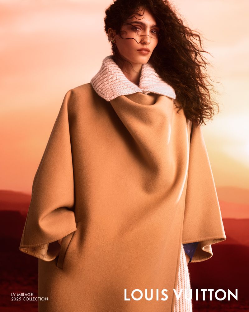 Fashion shot of a woman with dark curly hair wearing a tan coat with a knit collar, set against an orange and red gradient backdrop.