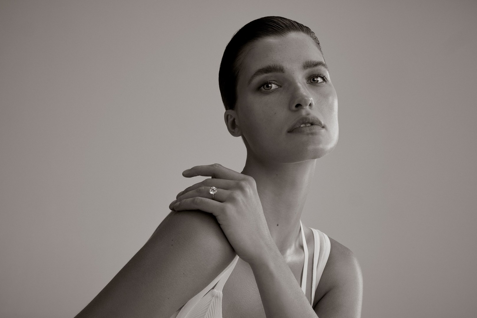 Close-up portrait of a woman wearing a ring on her shoulder while posing against a light grey background