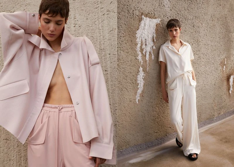 Two women in neutral loungewear posing against a textured wall in a fashion editorial shot with natural lighting and soft focus.