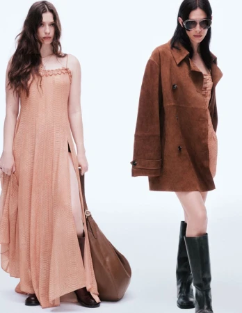 Two adult women model contemporary fashion in a bright photo studio, one wearing a long brown dress and boots, the other a brown coat.