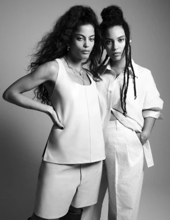 Monochrome portrait of two female models in white outfits against a plain grey studio backdrop
