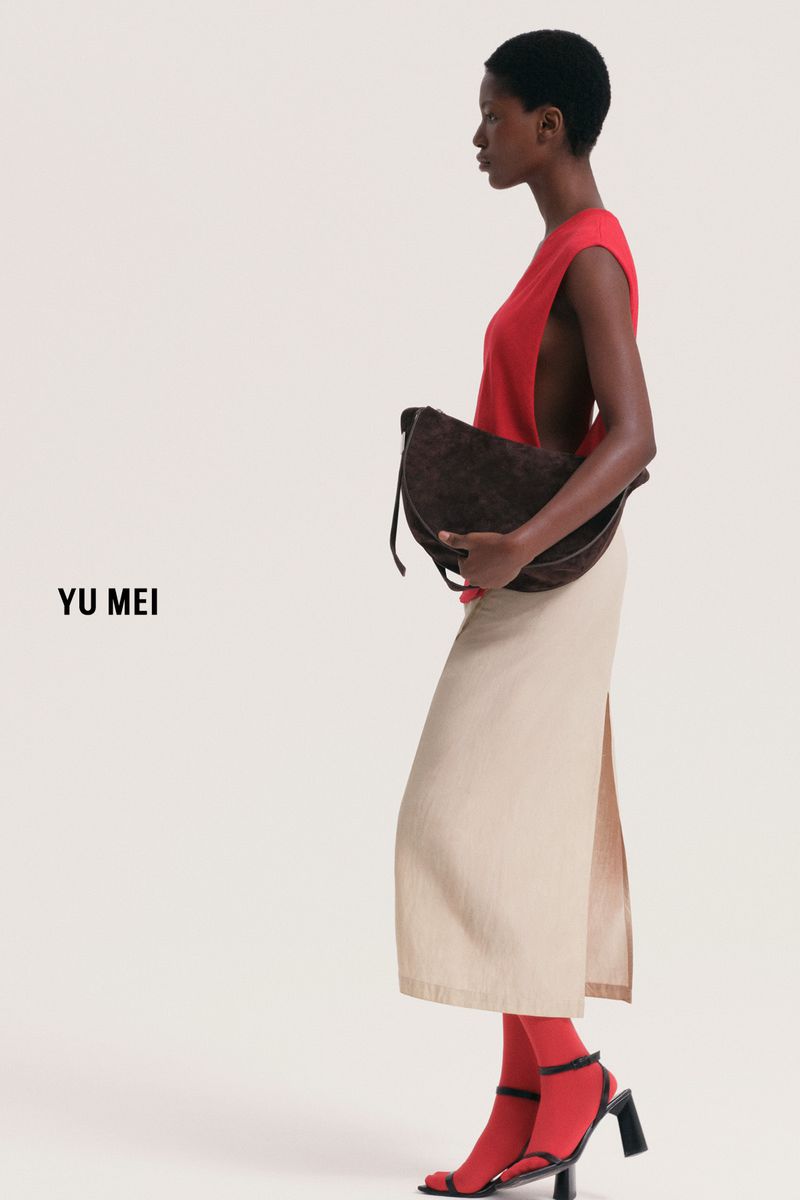 Fashion editorial shot of a Black female model in a sleeveless red top, beige skirt, brown purse, and red hosiery posing in studio.