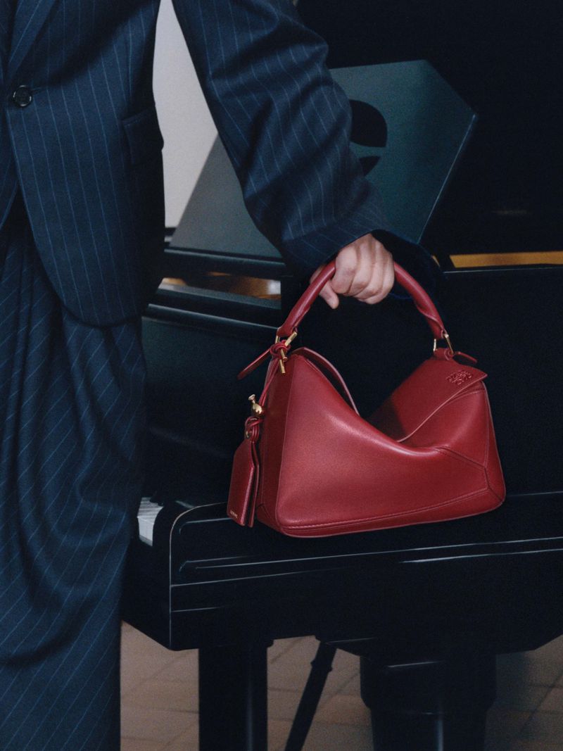 Fashionable red leather handbag is held in front of a black piano, accessorizing a pinstripe suit for a stylish, elegant look.