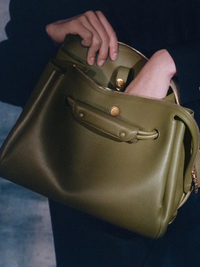 Close-up of hands opening an olive green leather handbag for the Loewe S/S 25 collateral campaign.