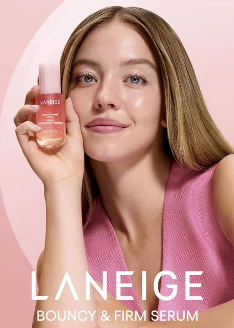 A blonde woman in a pink top holds a Laneige Bouncy & Firm Serum bottle, showcasing beauty and skincare in a close-up, studio setting.