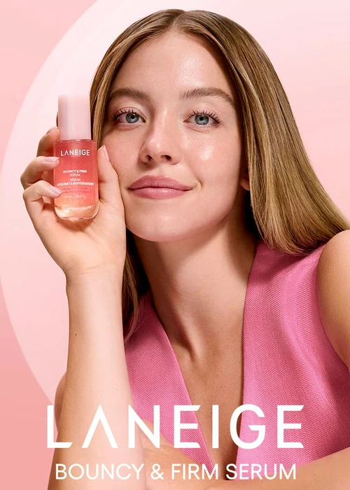 Sydney Sweeney holding a pink Laneige serum bottle in front of a soft pink studio background