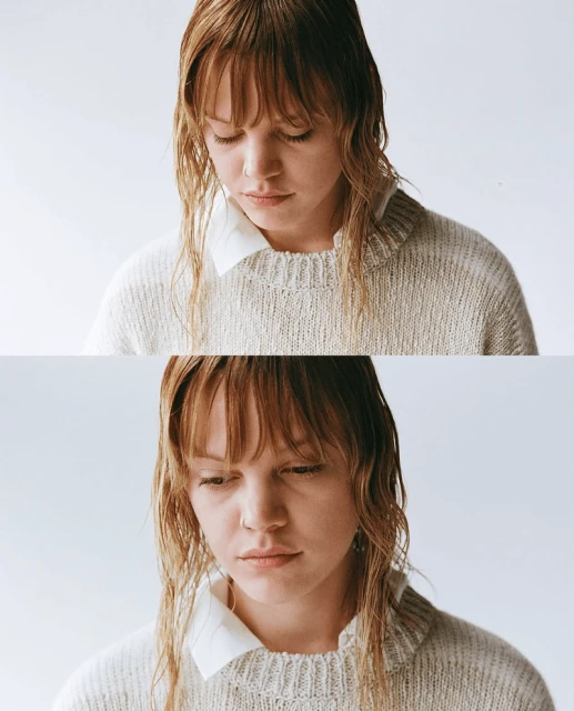 Portrait of a young adult woman with wet reddish-blonde hair wearing a sweater and white collared shirt, looking down in a studio.