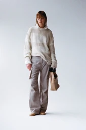 Model wearing cream striped knit sweater and grey cargo trousers holding a tan handbag against a white background.