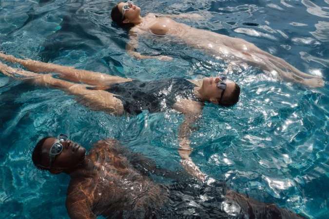 Three people float in blue water. One African-American man and two white women are submerged in a swimming pool on a sunny day.