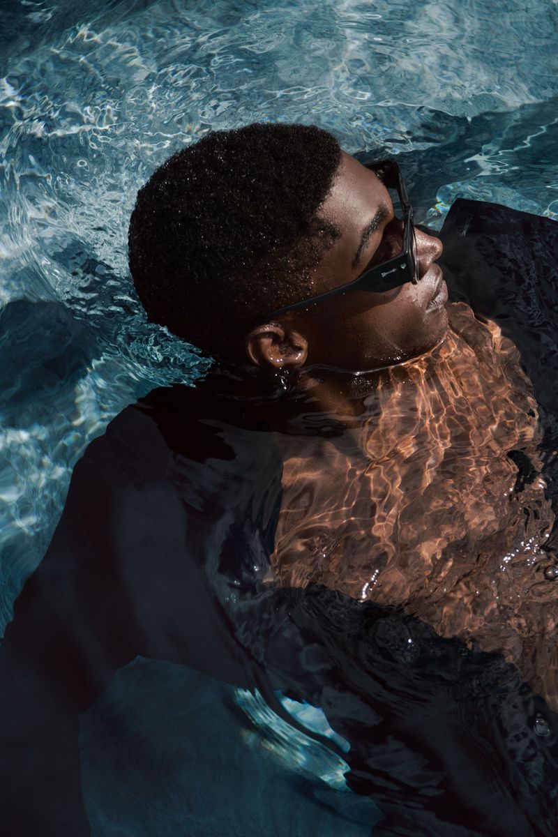Portrait of an adult male wearing sunglasses floating in turquoise-tinted water with light reflections, creating a serene and relaxed scene.