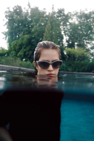 Model wearing dark sunglasses submerged in an outdoor pool with water level at chin height
