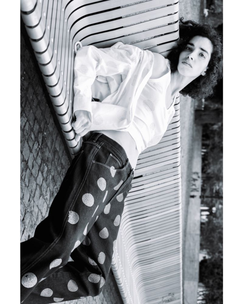 Woman lying on a modern bench wearing polka dot jeans and a white shirt in a black and white outdoor fashion shot.