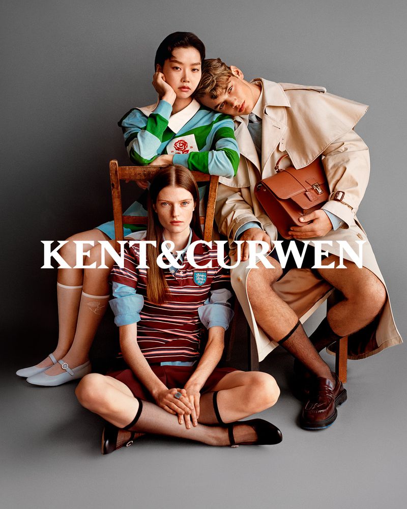 Fashion shoot featuring three models wearing preppy-style outfits, one seated on a wooden chair in a studio with a gray backdrop.