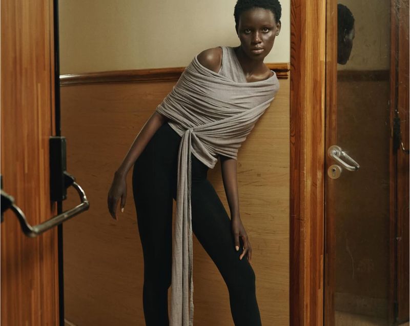 Fashionable African woman posing in form-fitting black leggings and a draped wrap top in a warm indoor setting, fashion editorial