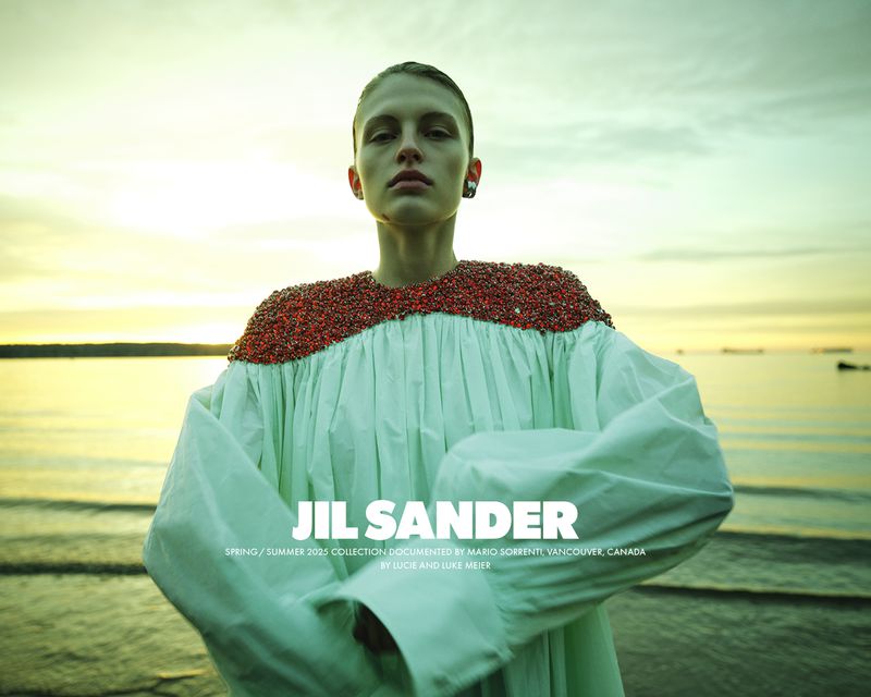 Fashion editorial shot of a fair-skinned woman in a dress with beaded shoulders standing by the ocean at sunset for JIL SANDER.