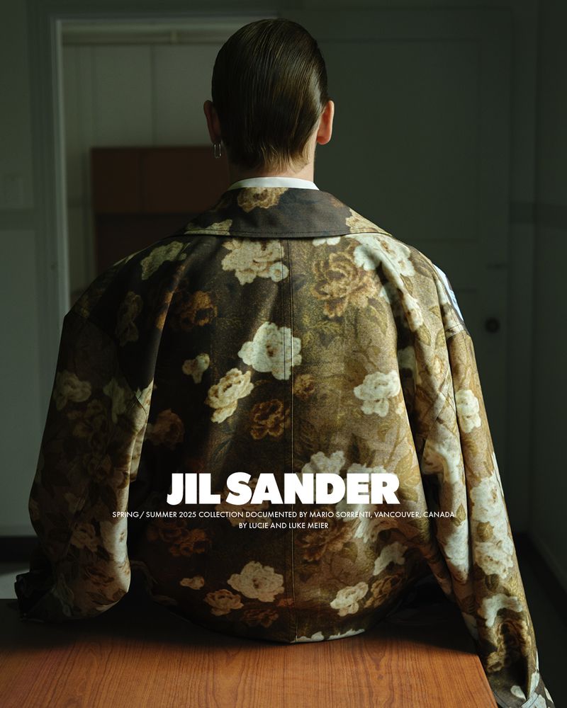 Back view of a person wearing a floral pattern jacket standing indoors in front of a brown table and a neutral color wall.