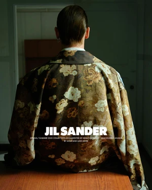 A model from the back wearing a floral patterned jacket seated indoors against a doorway in soft lighting.