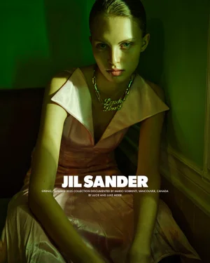 Model in a pale pink dress wearing a chunky gold chain necklace under green lighting for Jil Sander S/S 2025.