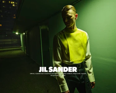 Model wearing a white shirt with bright yellow front panel standing in an exterior urban corridor at night with green ambient lighting.