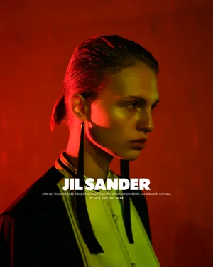 Portrait of a model with slicked-back hair and long earrings under dramatic red and green lighting for Jil Sander.