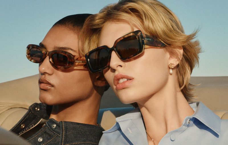 Two models wearing tortoiseshell sunglasses against a clear blue sky background