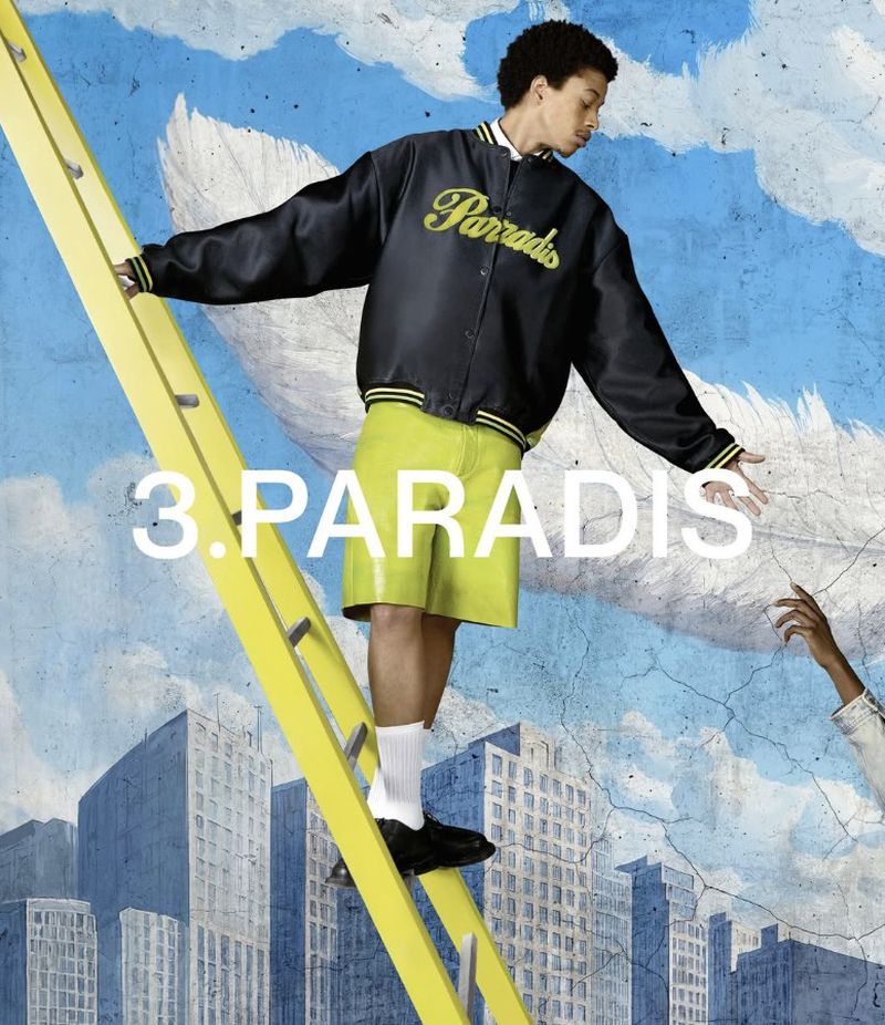 A person stands on a ladder in front of a city backdrop wearing a black jacket and lime green shorts in a fashion-forward pose.