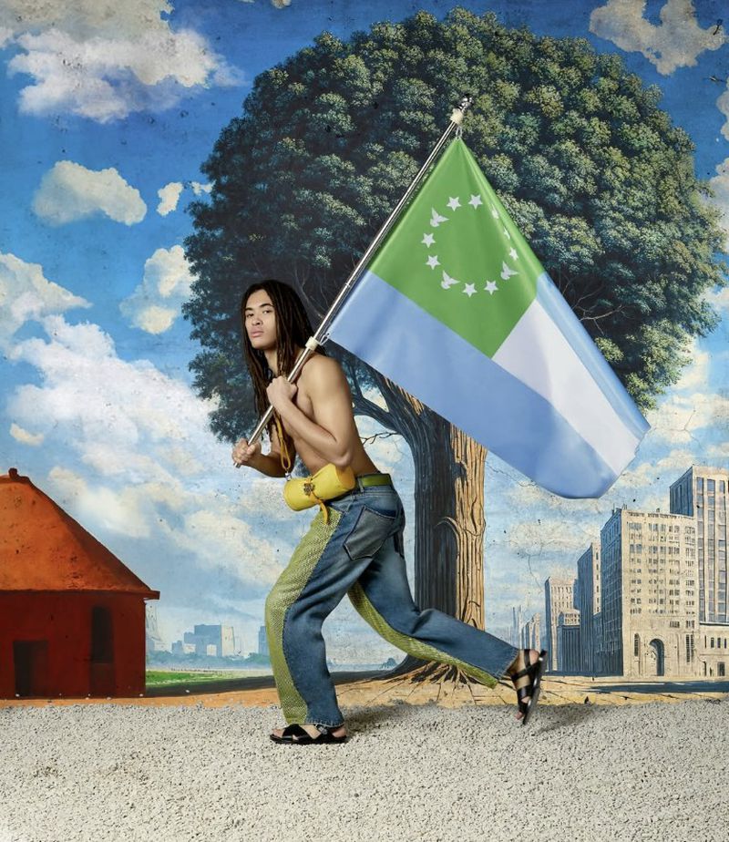 Man walking with a flag in an outdoor scene with a building backdrop. The flag has green and light blue colors with star design.