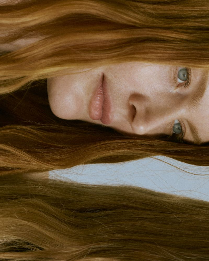 Close-up portrait of a young fair-skinned woman with blue eyes and long red hair. Beauty shot, focusing on facial features and hair.