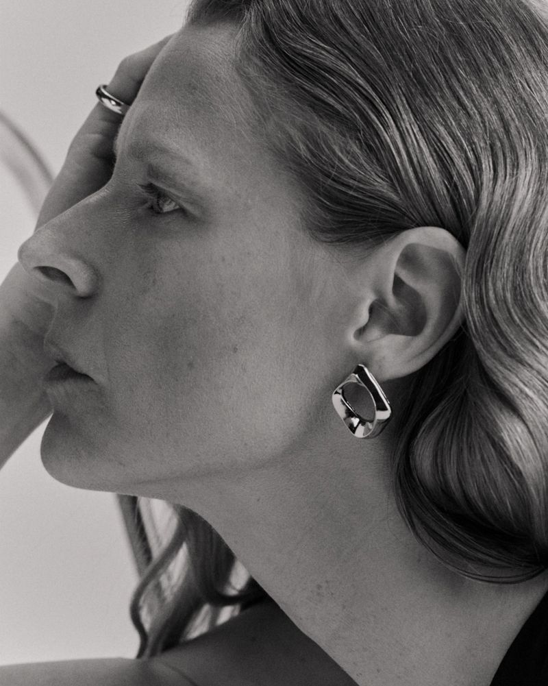 Monochrome portrait of a woman with silver earrings, her hand near her face, showcasing a beauty and fashion aesthetic.