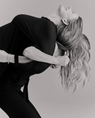 Monochrome image featuring two adult women in close embrace; one in black top and pants, the other with long blonde hair.