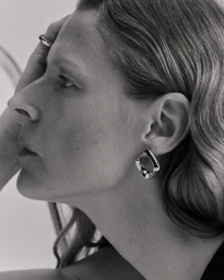Close-up profile portrait of a woman wearing a metallic earring and ring against a plain light background