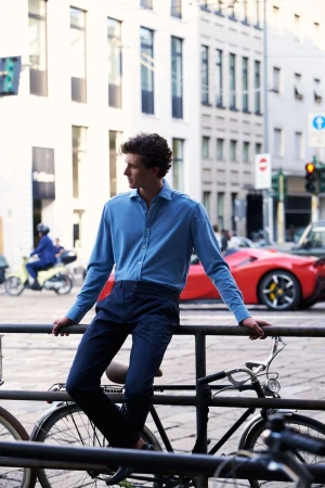 Man in blue shirt leans on railing with bicycles in an urban setting, with a red sports car visible in the background on a sunny day.