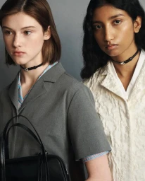 Two female models wearing thin black chokers and structured collared shirts against a plain grey studio background.